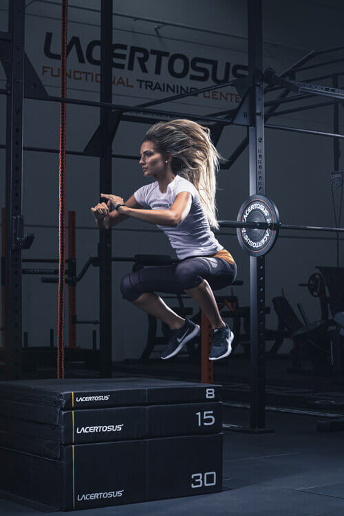 Mujer realizando un salto pliométrico sobre cajas de diferentes alturas en el gimnasio.