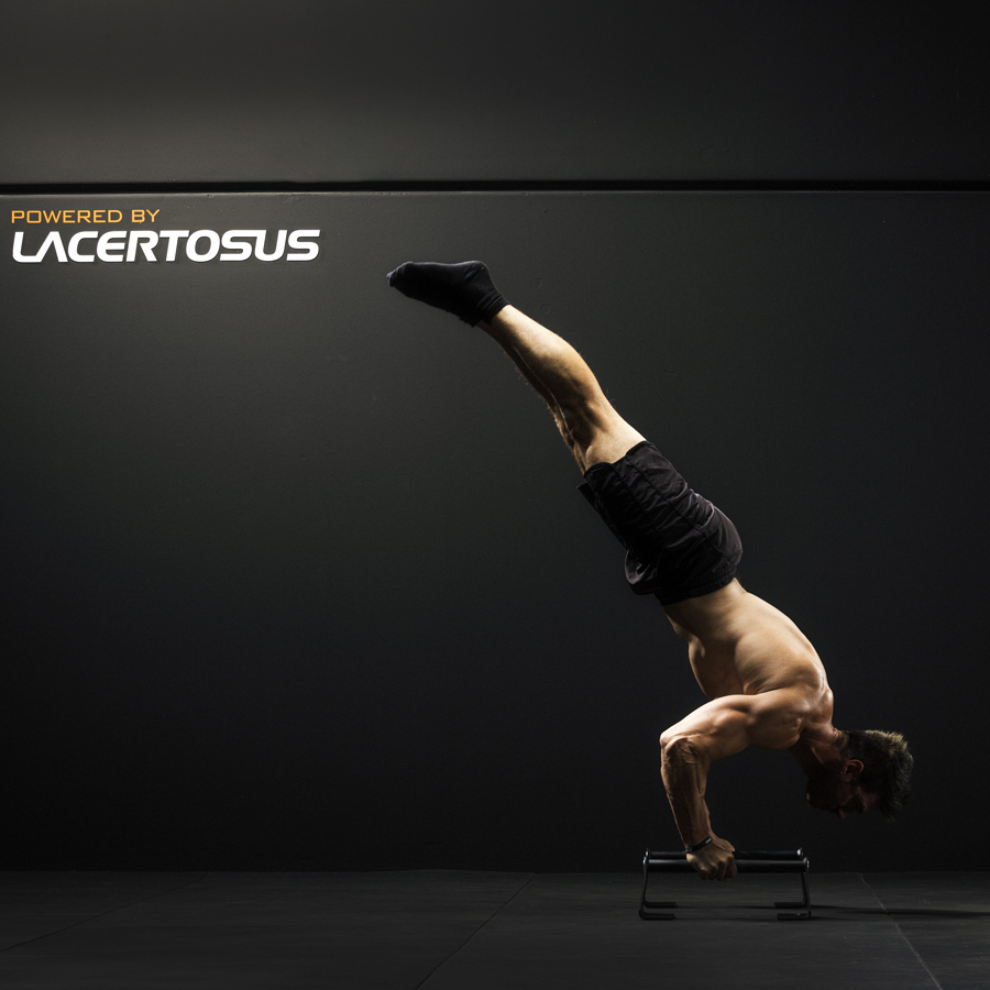 Un hombre realiza una parada de manos sobre paralelas en una habitación oscura.